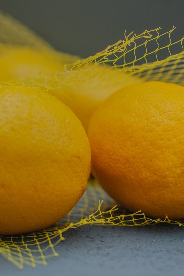 Желтые лимоны в сетке на сером столе