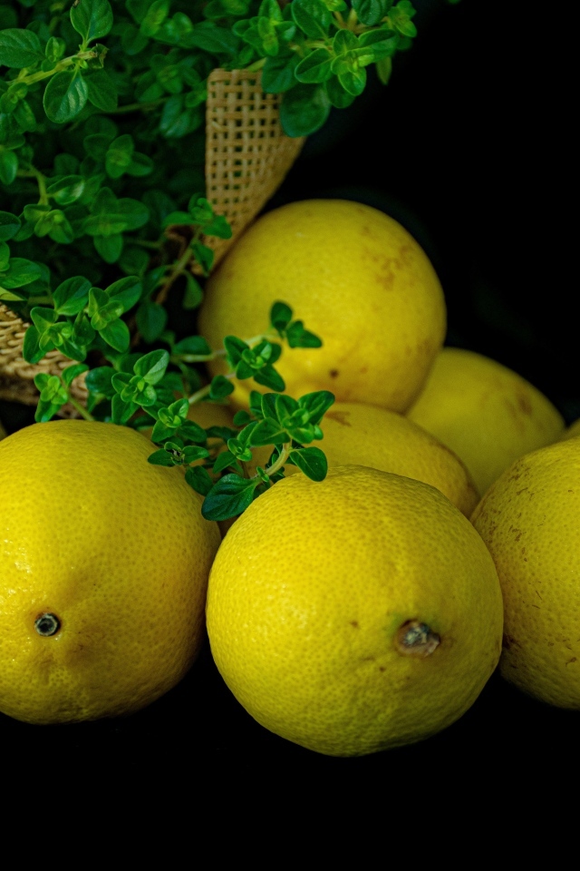 Желтые лимоны на черном столе с зеленью