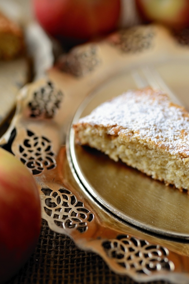 Кусок пирога с сахарной пудрой на столе с яблоками