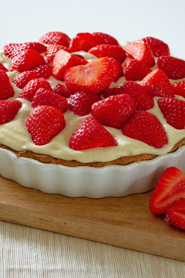 Большой пирог с кремом и ягодами спелой клубники на столе