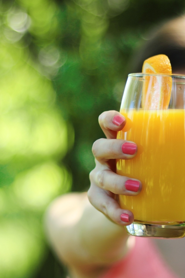 Девушка держит стакан апельсинового сока в руке