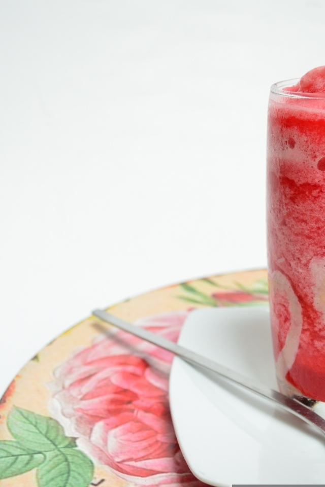 Стакан красного ягодного смузи на столе с чайной ложкой