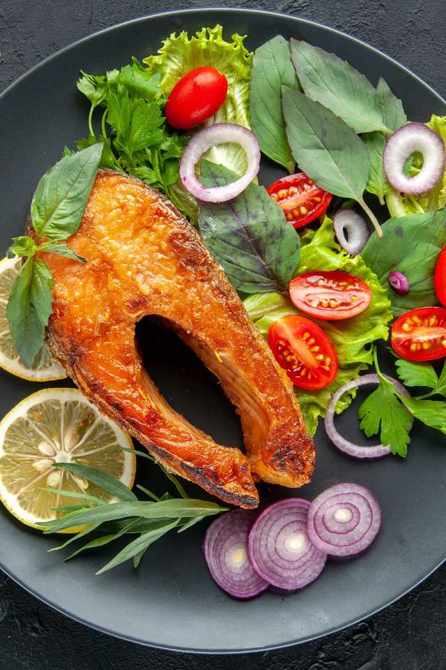 Жареная рыба на тарелке с зеленью,  лимоном и помидорами