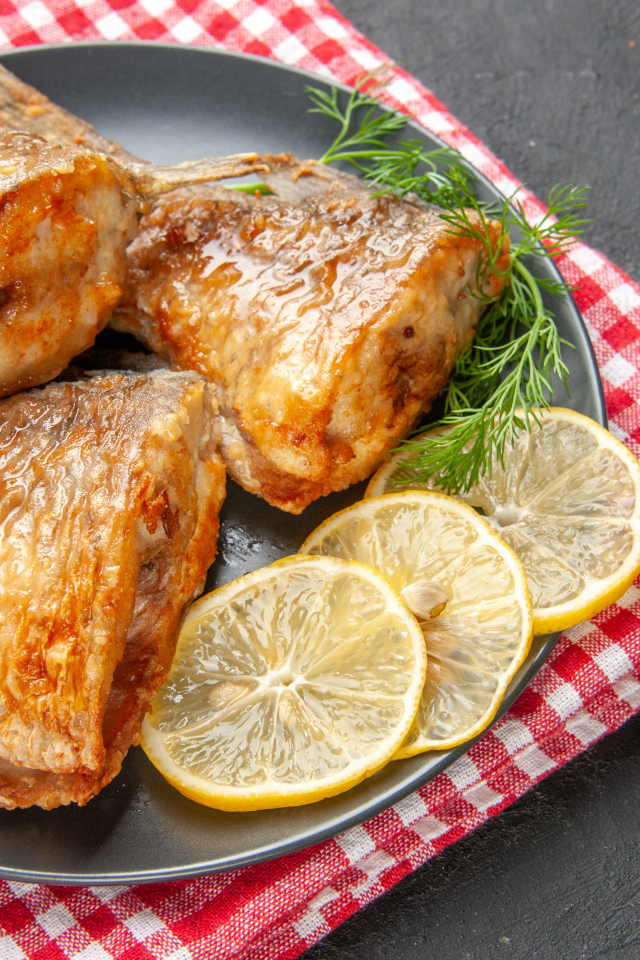 Куски жареной рыбы на тарелке с кусочками лимона и укропом