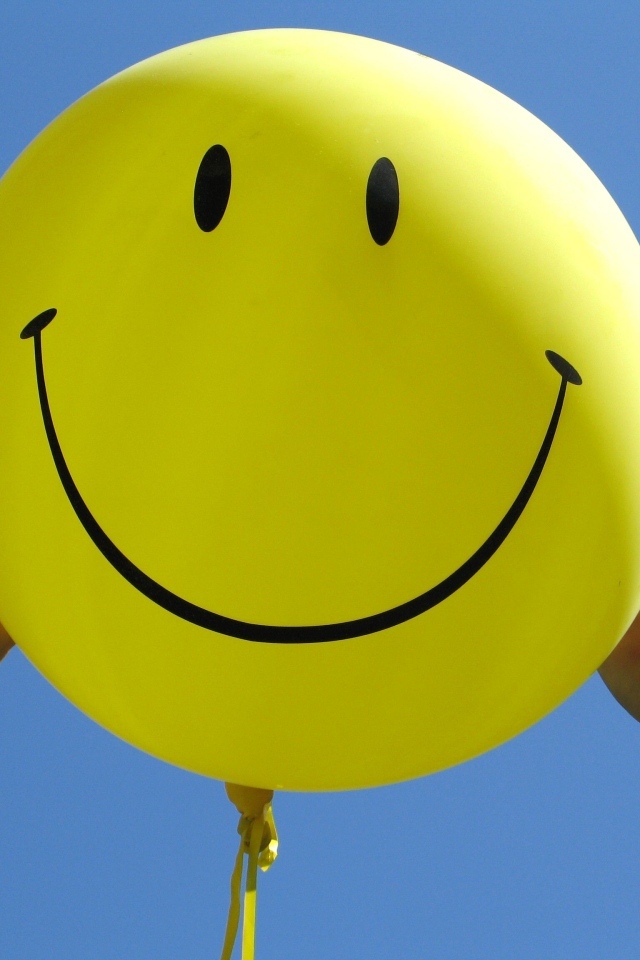 Желтый шарик с улыбкой в руках на голубом фоне