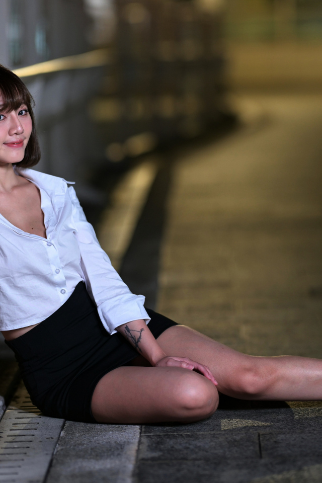 Девушка в черной юбке и белой рубашке сидит на дороге