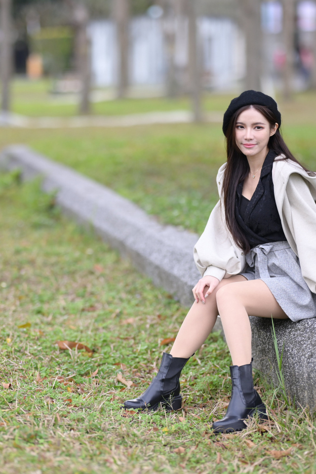 Девушка в пальто сидит на земле в парке