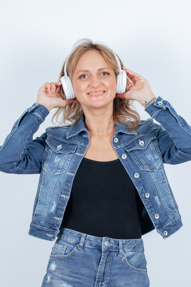 Девушка в джинсовом костюме с наушниками на голове на фоне стены