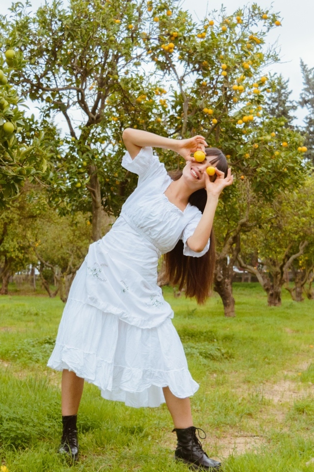 Девушка в белом платье закрыла глаза лимонами