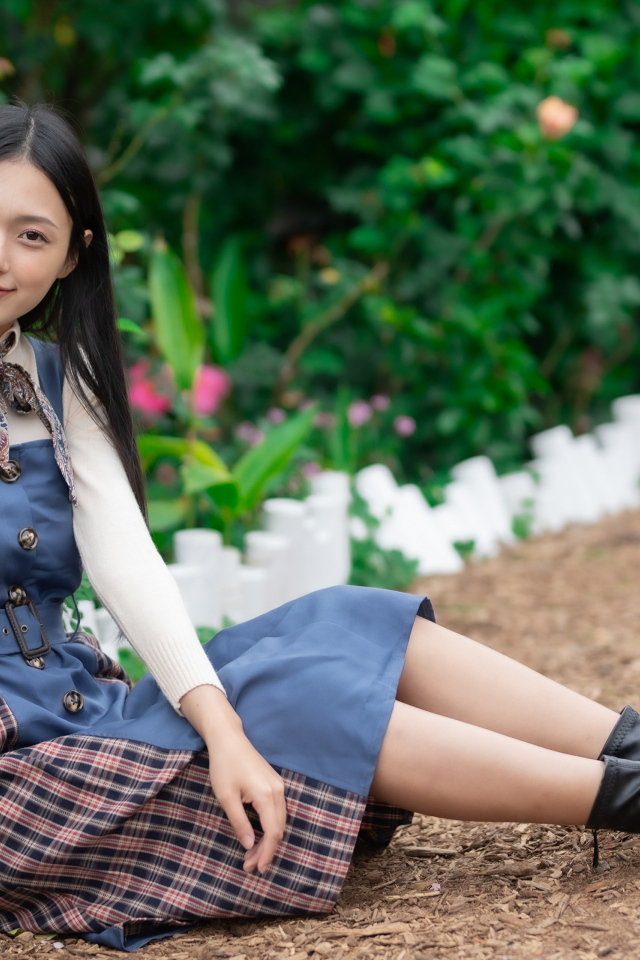 Молодая девушка сидит на тропинке у клумбы