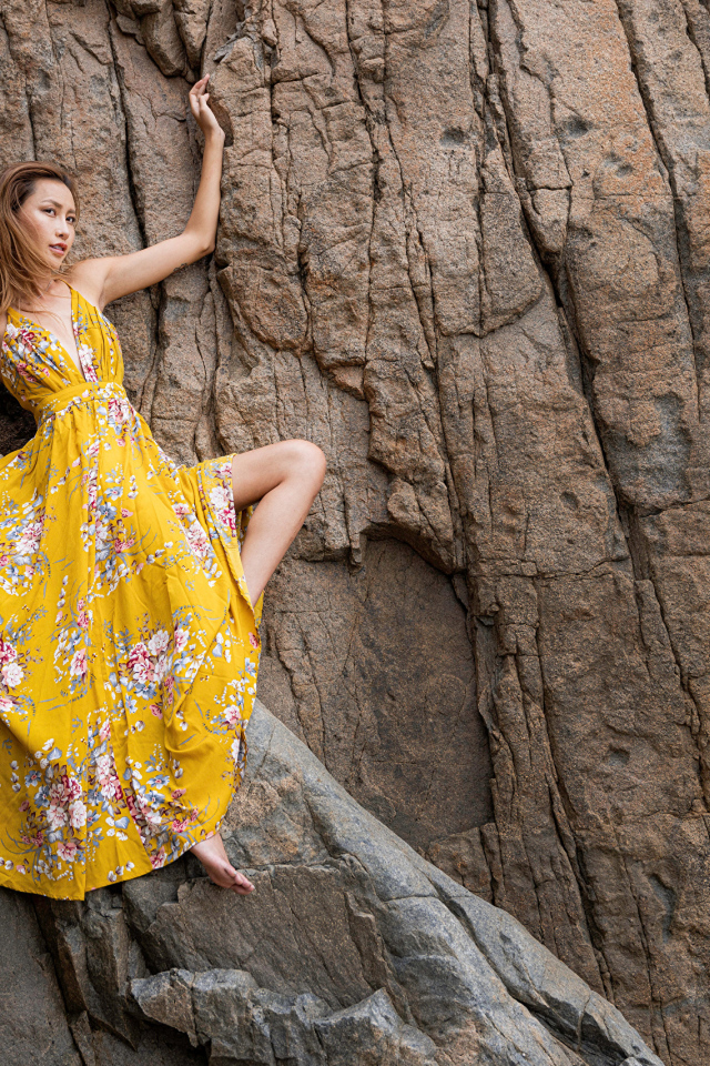 Девушка азиатка в красивом длинном платье позирует на скале