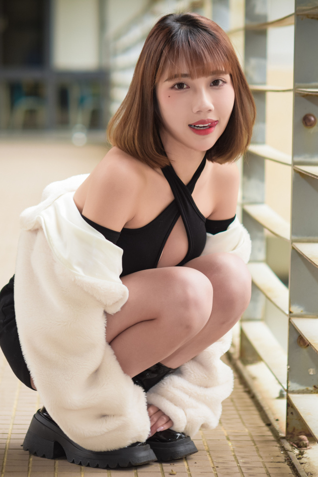 Девушка азиатка в белой шубе сидит на корточках