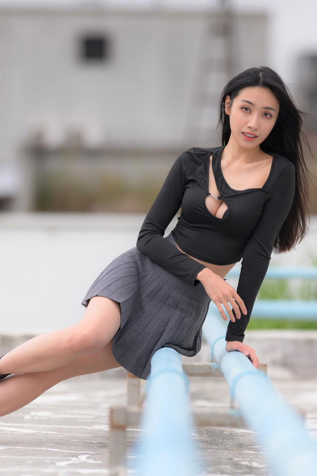 Девушка азиатка в черном наряде сидит на трубе