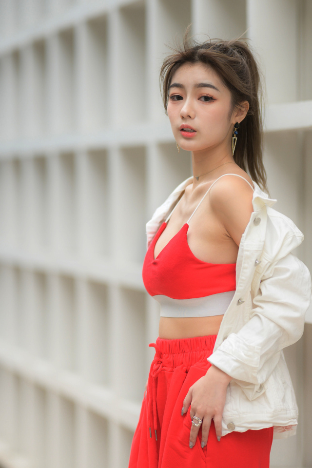 Азиатка в красном спортивном костюме стоит у стены