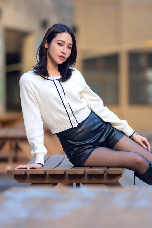 Азиатка в черных кожаных сапогах лежит на деревянном столе