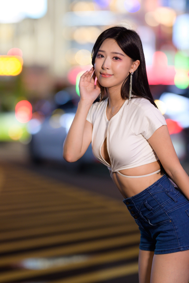 Азиатка в коротких шортах стоит на дороге в городе
