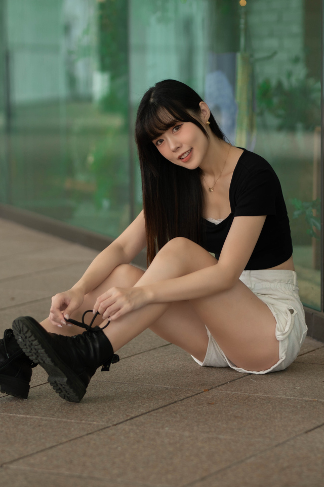 Азиатка в шортах сидит у стеклянной стены