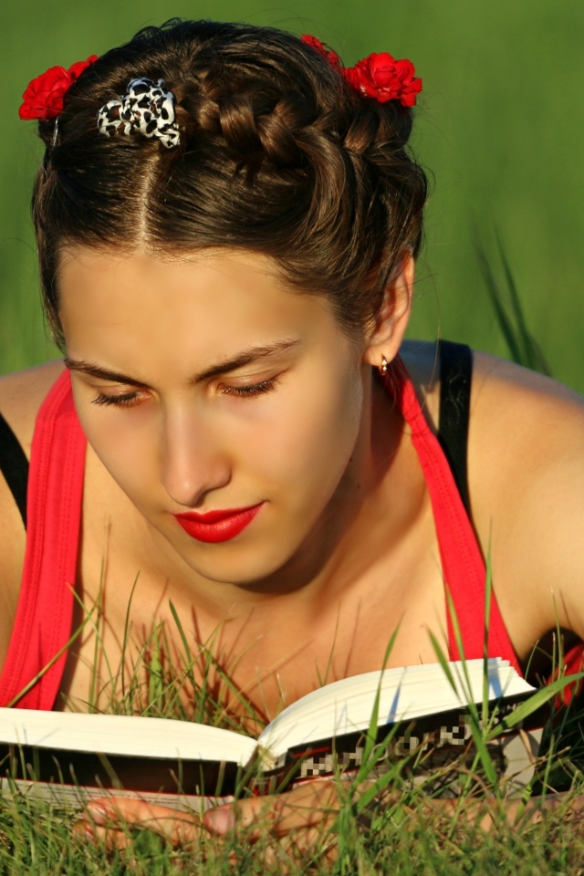 Красивая девушка читает книгу лежа на траве