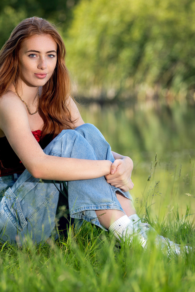 Красивая рыжеволосая девушка сидит в зеленой траве