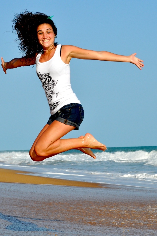 Веселая девушка прыгает на морском берегу