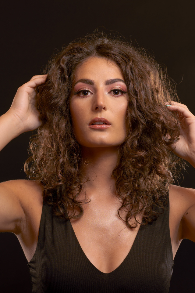 Кудрявая девушка держит руки в волосах на черном фоне