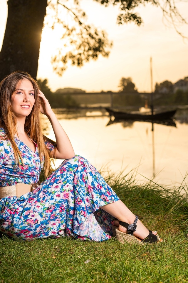 Милая девушка в платье сидит на берегу реки в парке