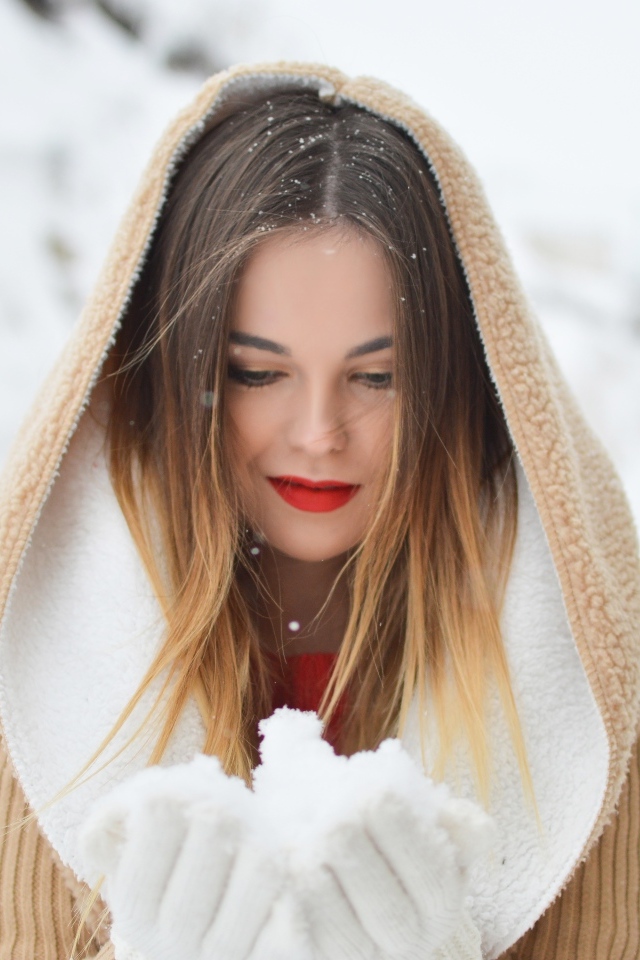 Милая девушка в капюшоне держит снег в ладонях