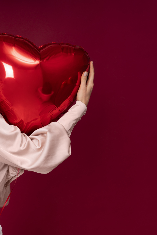 Девушка держит шарик в форме сердца на красном фоне