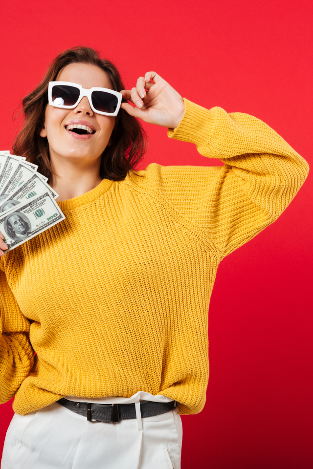 Девушка с веером из долларов на красном фоне