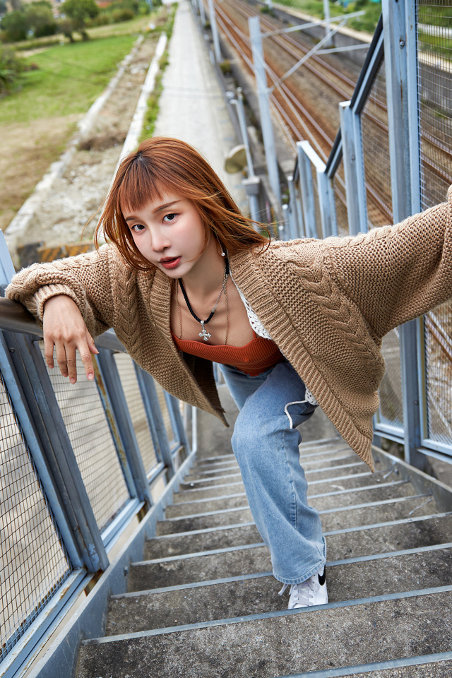 Рыжеволосая азиатка в кофте стоит на ступеньках