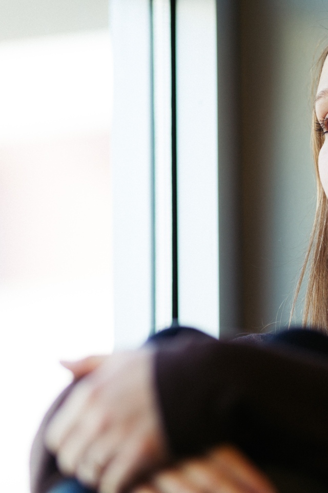 Грустная девушка сидит у окна