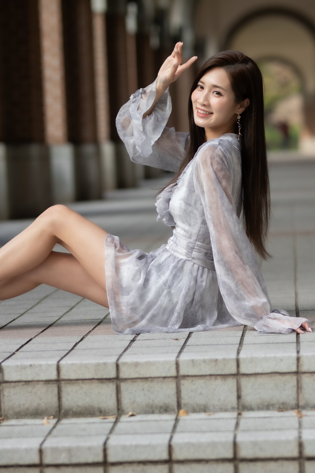 Улыбающаяся девушка азиатка сидит у ступеней