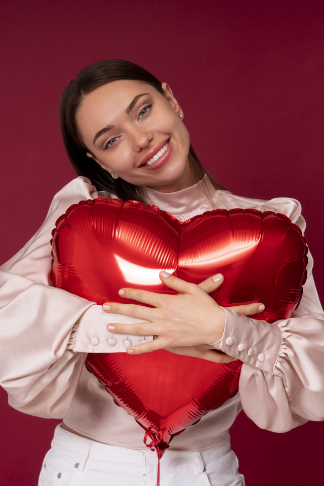 Улыбающаяся девушка обнимает шар в форме сердца