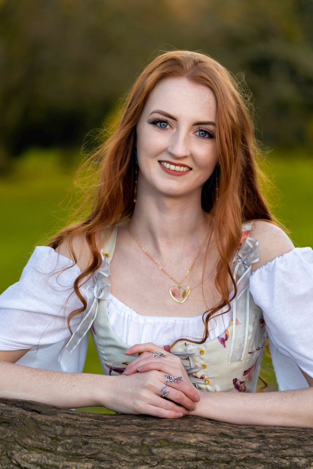 Улыбающаяся рыжеволосая девушка стоит у дерева