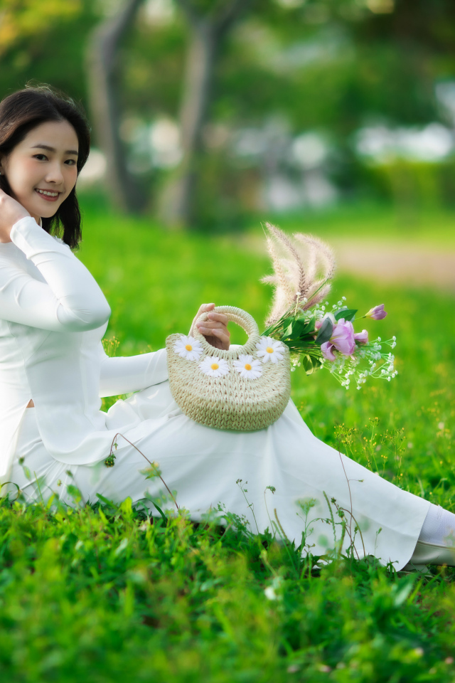 Нежная азиатка в белом наряде сидит на траве
