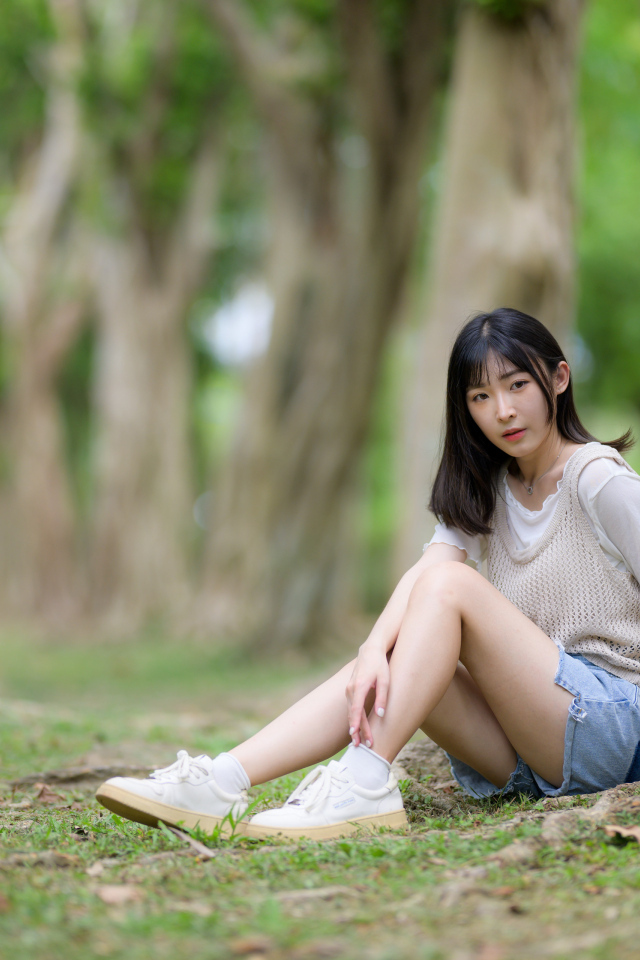 Молодая девушка азиатка сидит у дерева в парке