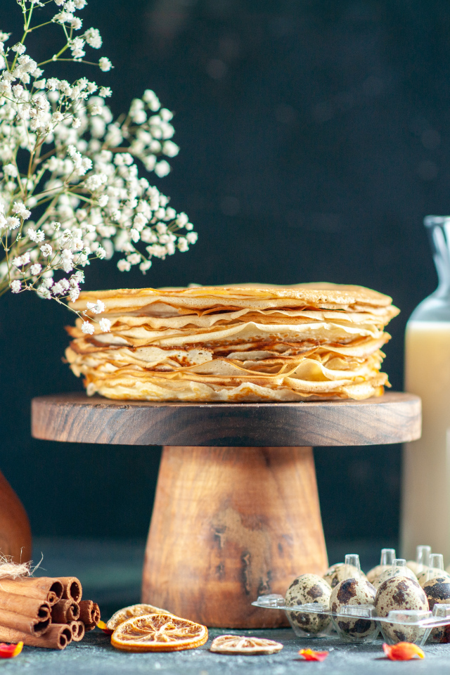 Тонкие блины на столе с молоком, букетом цветов и специями