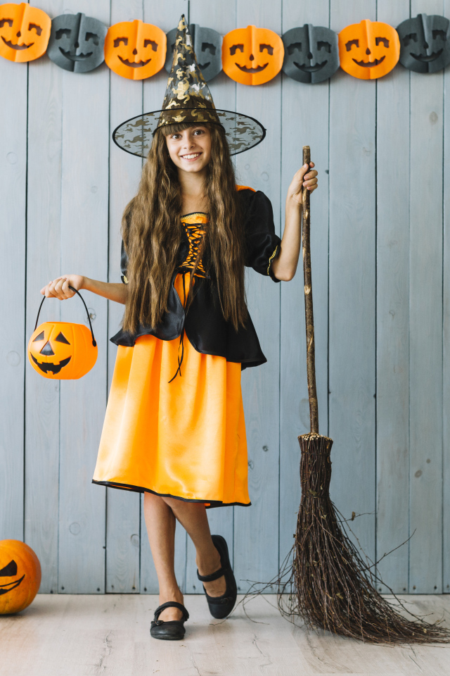 Девочка в костюме ведьмы у стены с декором на Хэллоуин