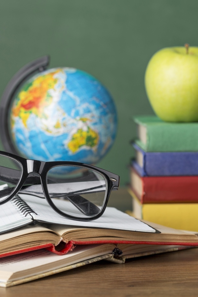 Книги, очки и карандаши с глобусом на столе у доски