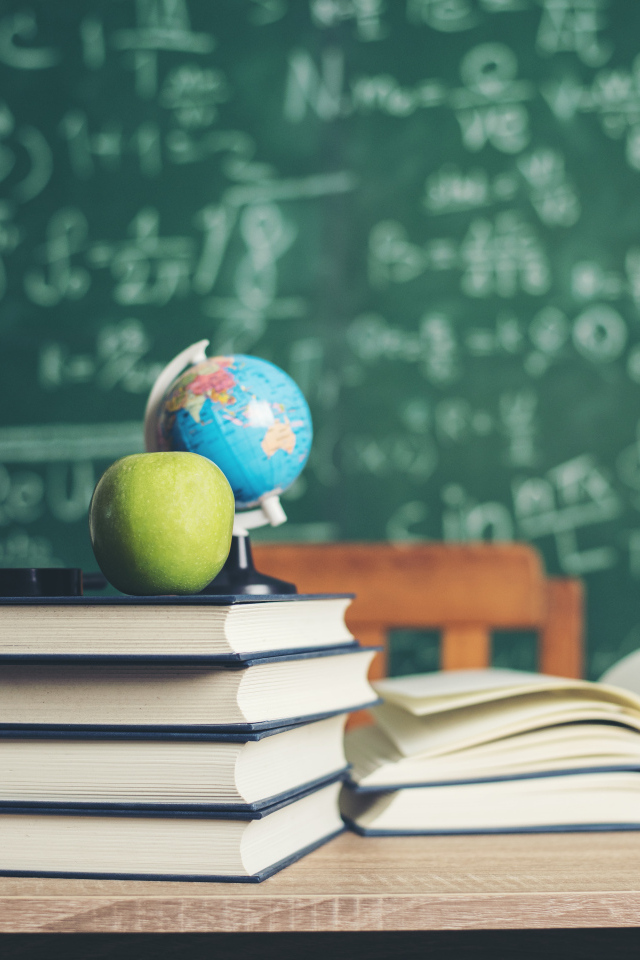 Книги на столе с зелеными яблоками и глобусом на фоне доски