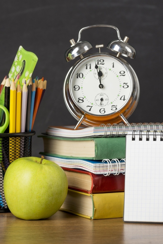 Канцелярские предметы на столе с будильником и книгами 