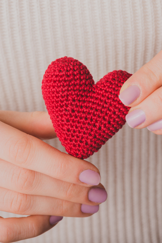 Девушка держит в руке вязаное красное сердце