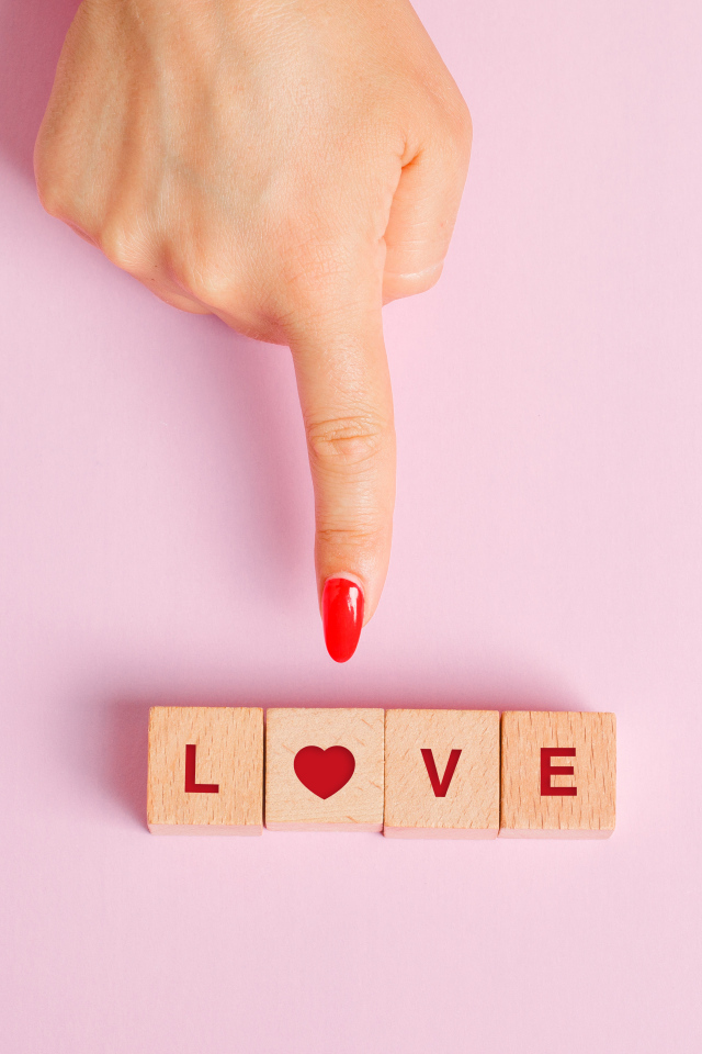 Рука указывает на кубики с надписью любовь на розовом фоне