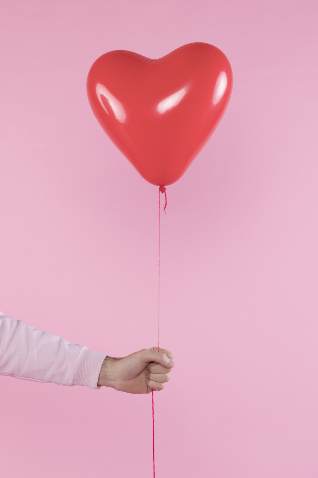Шарик в форме сердца в руке на розовом фоне