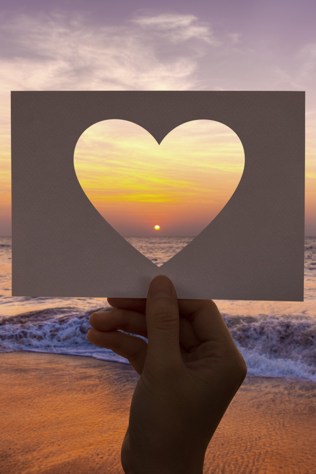 Бумажное сердце на фоне моря на закате солнца