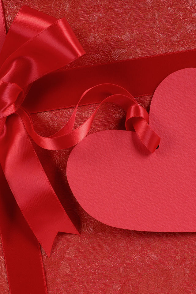 Бумажное сердце с бантом из атласной ленты на красном фоне