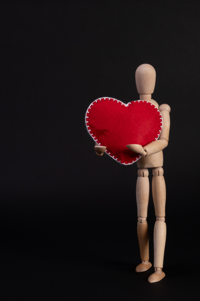 Марионетка держит красное сердце на черном фоне