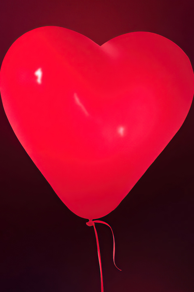 Красный шарик в форме сердца на фоне стены