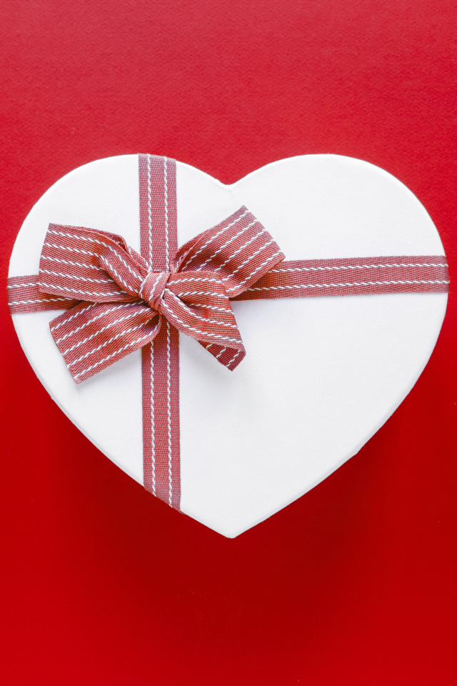 Белая коробка в форме сердца с бантом на красном фоне
