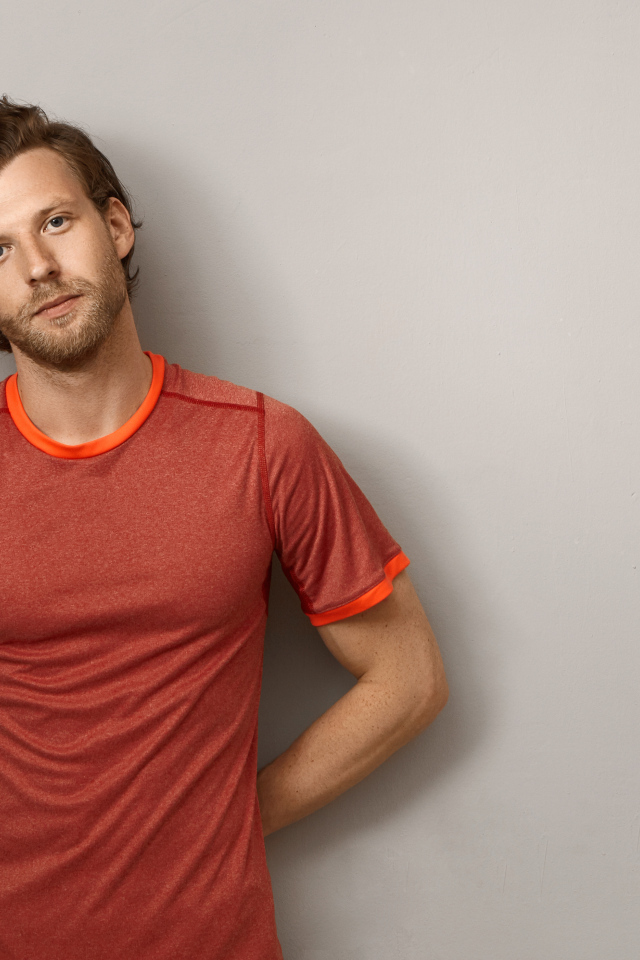 Мужчина в футболке стоит у серой стены